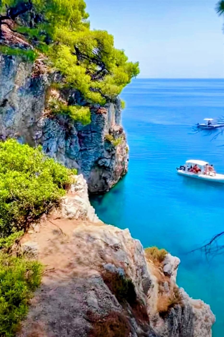 Pine-topped cliffs above a turquoise cove with visiting boats