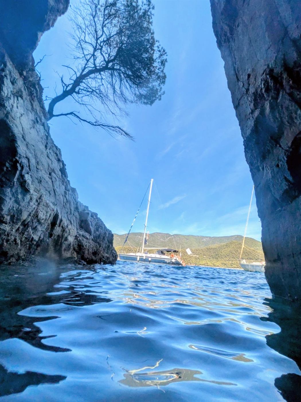 Sea cave opening onto a bay with a sailing yacht beyond